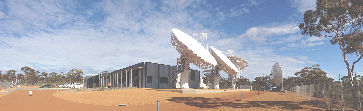 A satellite ground station with large satellite dishes in regional Australia with red dirt, blue sky and surrounding trees