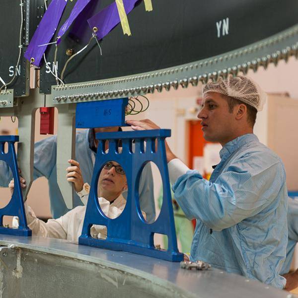 Three people are working on nbn's Sky Muster Satellite prior to it being launched into space