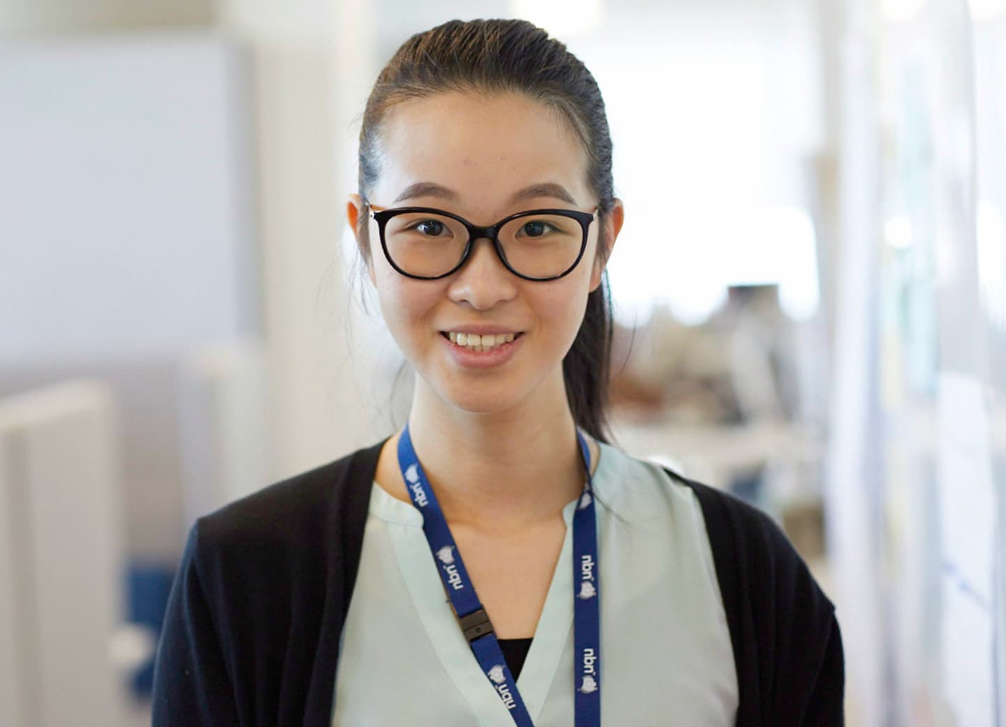 An nbn graduate is wearing an nbn lanyard while standing in a light-filled office smiling at the camera