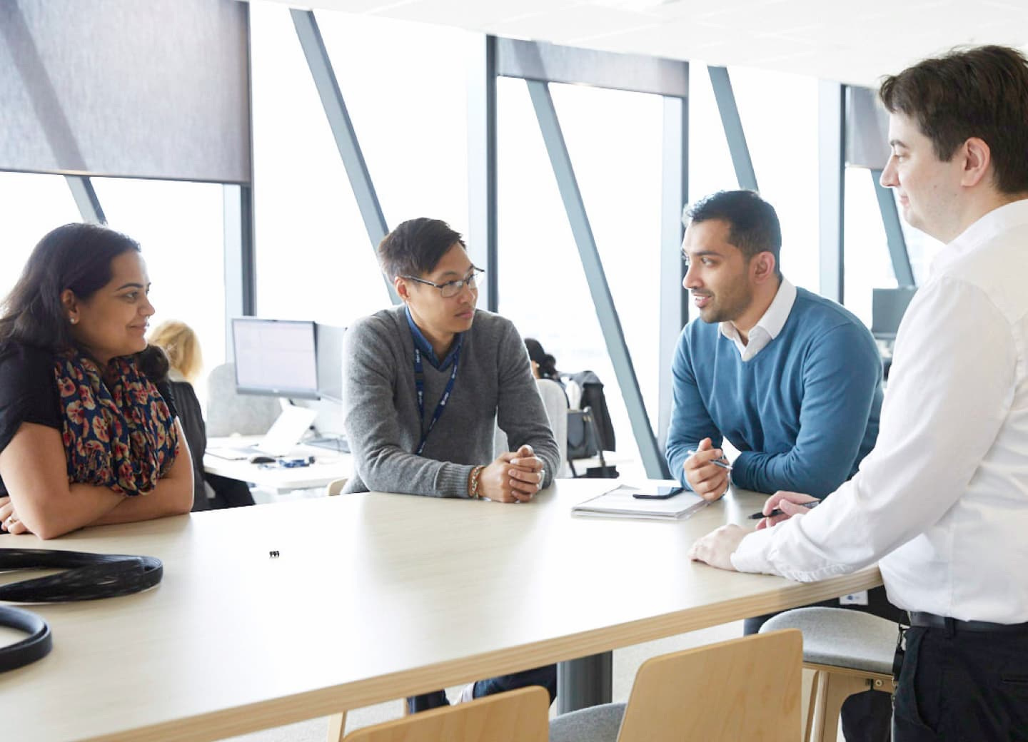 A group of nbn employees are talking around a meeting table in a light-filled office